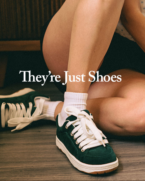 Person wearing green and white sneakers with text 'Simple. They're Just Shoes' on a wooden floor.